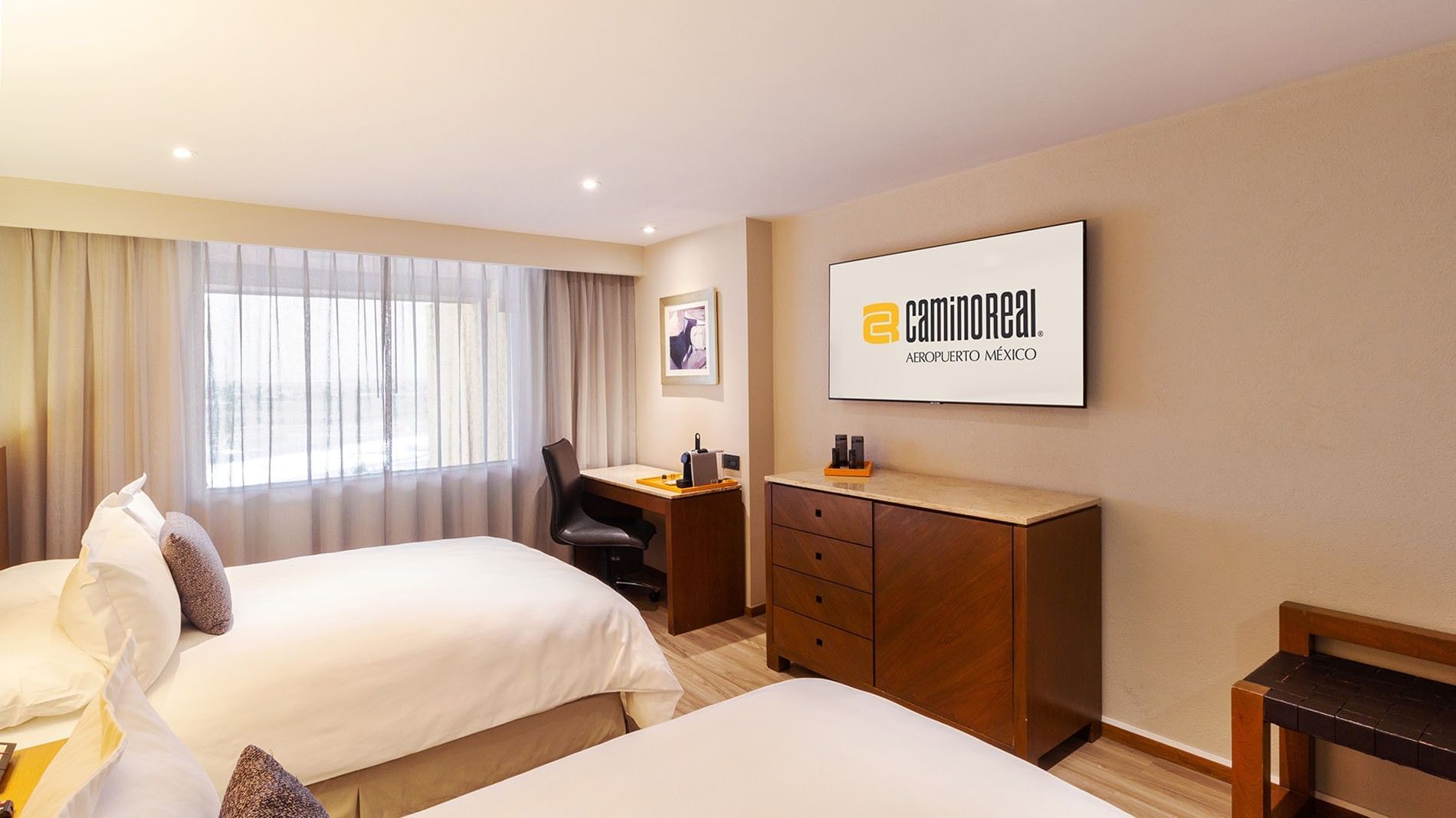 Habitación con dos camas dobles, escritorio y televisor en Camino Real Aeropuerto México, Ciudad de México.