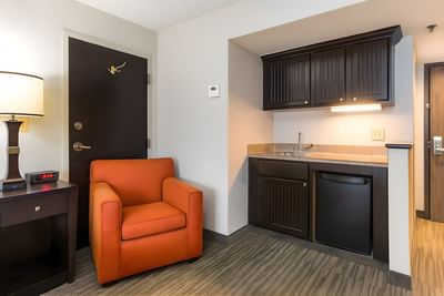 Standard King Room kitchenette area with dark cabinets, small sink, mini-fridge, and orange chair at Branson Hillside Hotel