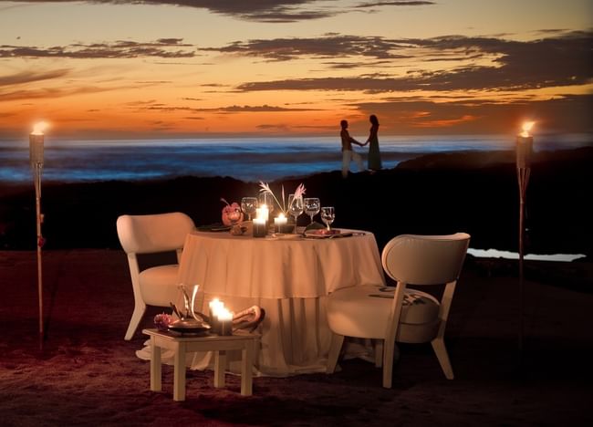Romantic candlelit dinner on the beach featuring a sunset view and tiki torches at Cala Luna Boutique Hotel