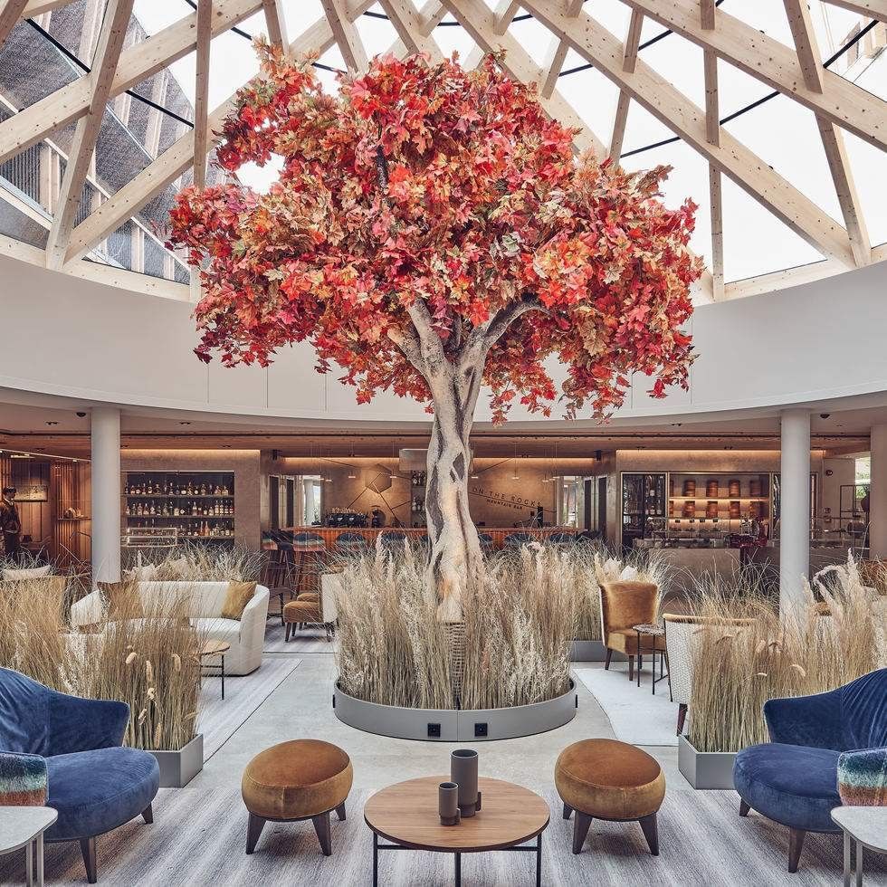 Großes künstliches rotes Baummodell in einer eleganten Lobby mit Sitzmöbeln und einer Glasdecke.