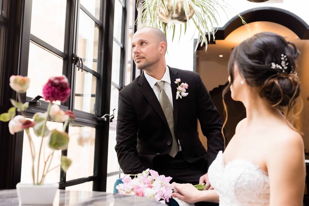 Groom gazes out a window while the bride sits nearby at El Prado Hotel