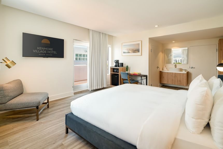 hotel room with white bedding, wood floors, desk, balcony access, and ensuite bathroom at Kenmore Village Hotel, South Beach