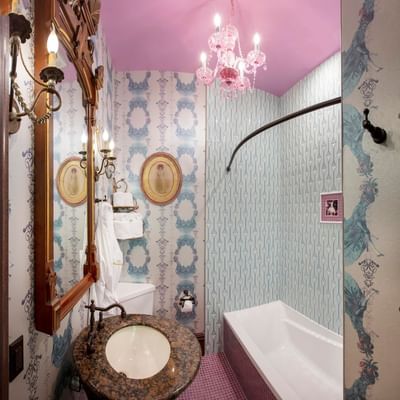 Bathroom with granite sink, vintage mirrors, pink chandelier, and bathtub in The Ghost and Mrs Hicks at The Roxbury