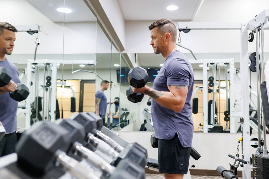 Man lifting weights in front of a mirror in fitness center at Rodd Royalty, one of the luxury hotels in Charlottetown, PEI