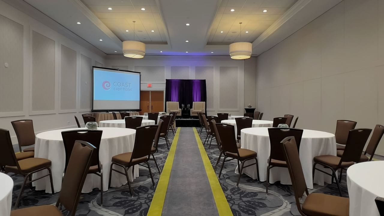 Ballroom with round tables, chairs, stage, podium and presentation screen