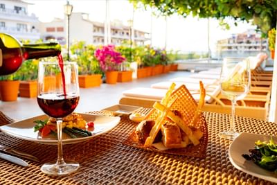 Red wine poured into a glass beside gourmet dishes on a woven outdoor dining table at Casa Dona Susana
