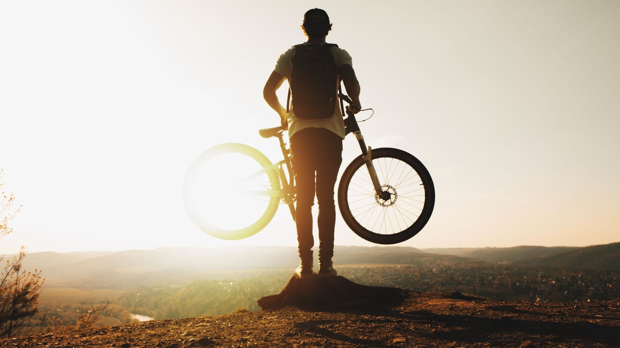 Boy on a cliff holding a bicycle at sunrise at Originals Hotels