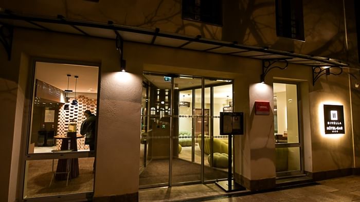 Entrée éclairée d'un hôtel de nuit avec un client à l'intérieur, Hôtel Rivella.