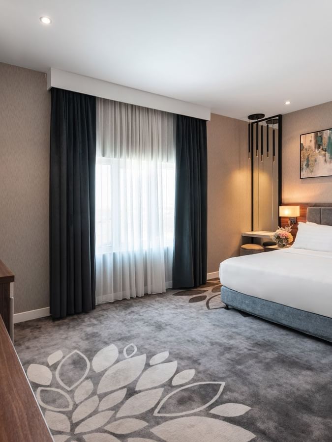 King bed by a large floral rug and a wooden console table with flowers in Executive Room City View at Warwick Al Jubail