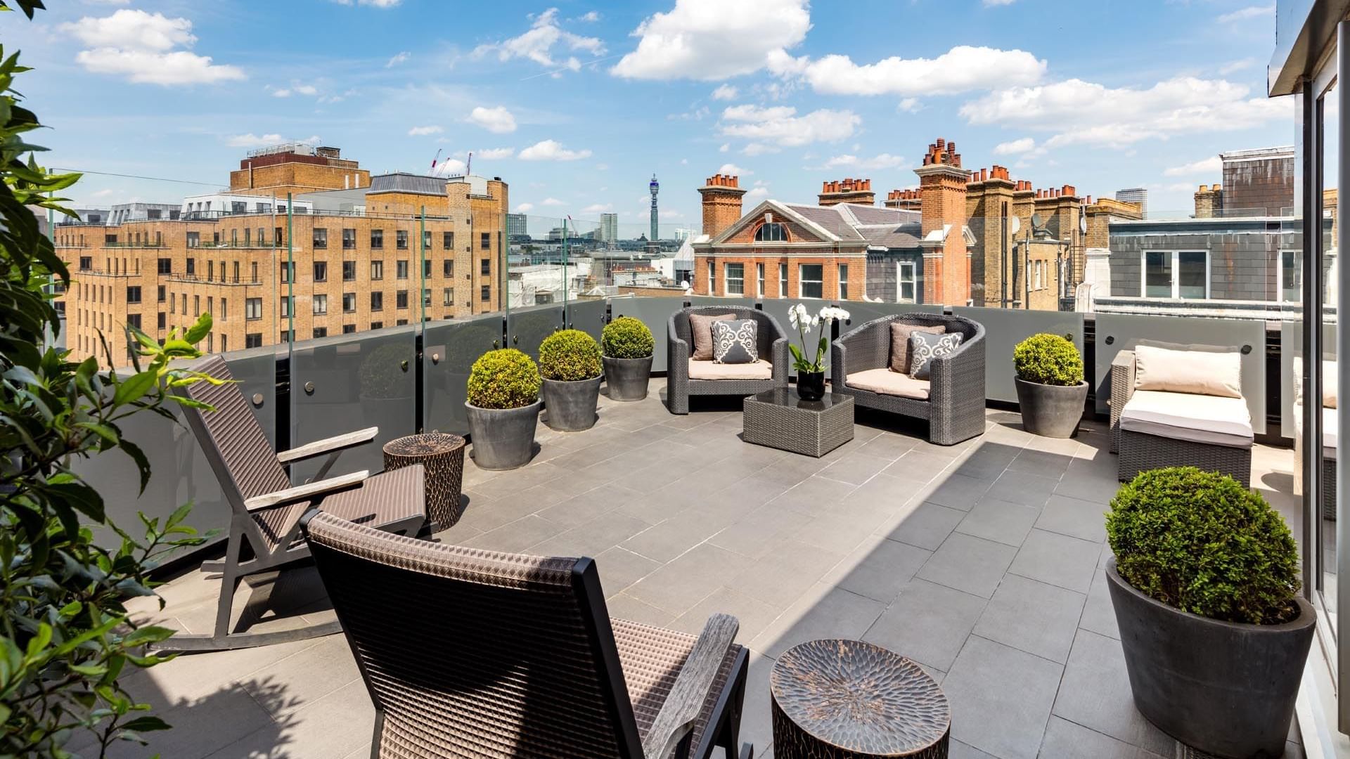 Rooftop patio in Ebony Suite at The May Fair Hotel London, featuring wicker chairs and sofas under a blue sky