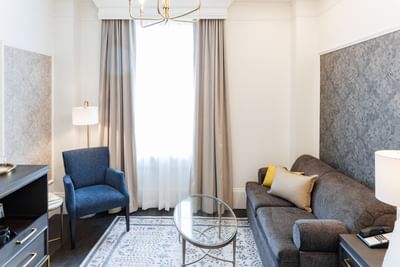 Executive One Queen Bed with blue armchair sits by a glass coffee table in front of a sofa at Rodd Charlottetown Hotel