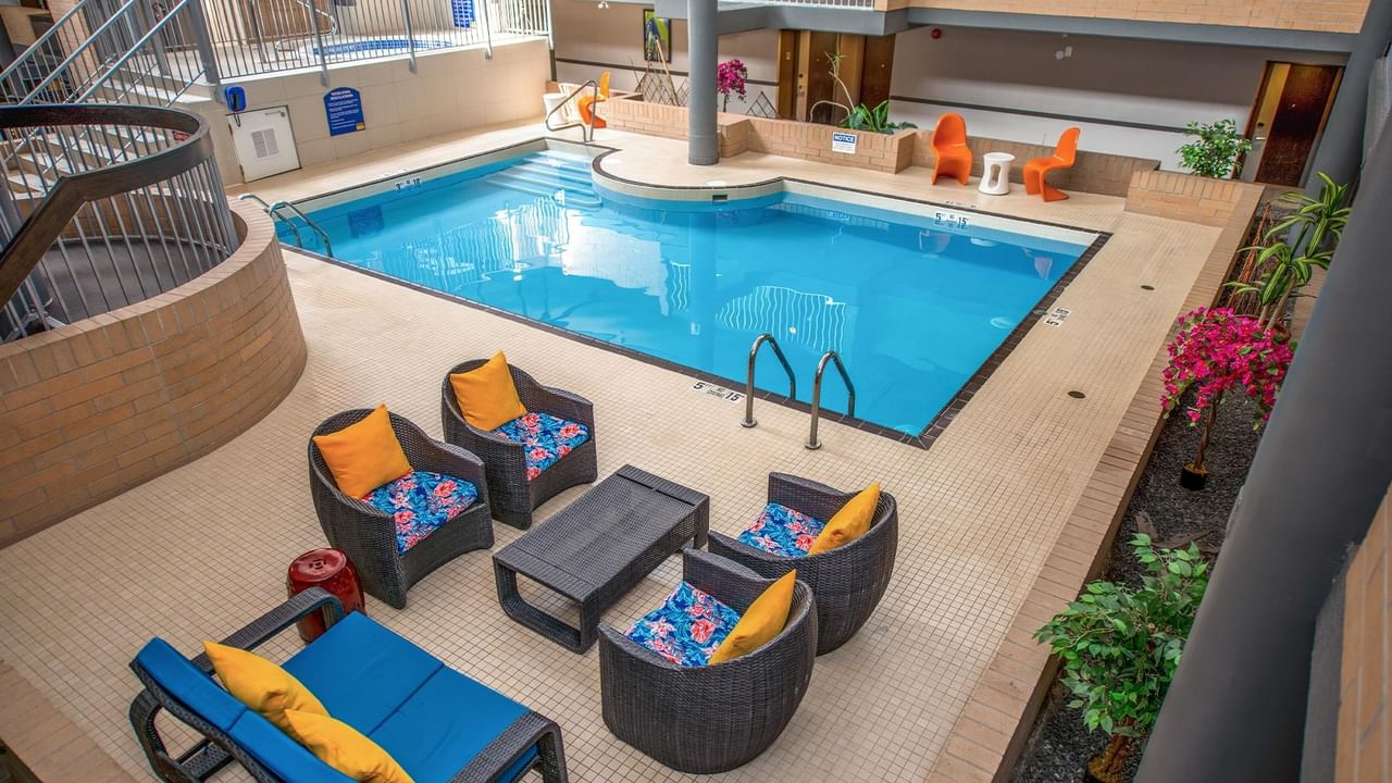 Indoor pool area with colorful lounge seating and vibrant plants at Coast Calgary University Area Hotel by APA