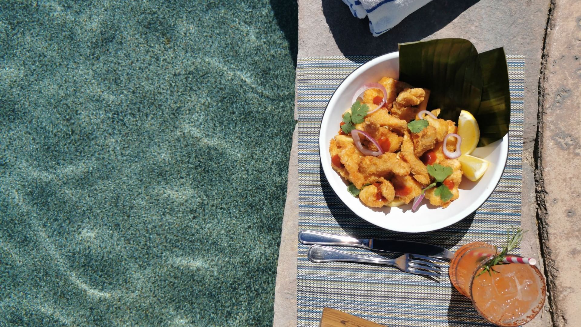 Bowl of fried seafood, a cocktail, and a rolled towel by the side of a Sirenas Restaurant pool at Hacienda del Mar Los Cabos.