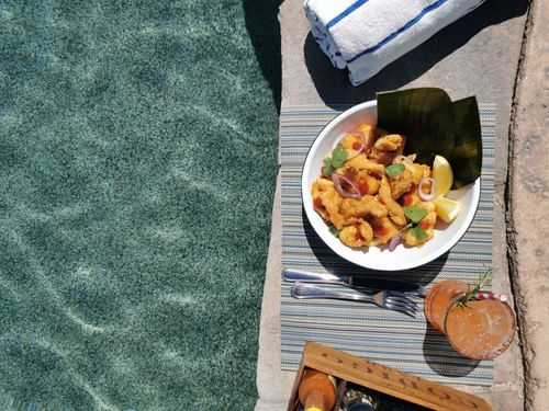 Bowl of fried seafood, a cocktail, and a rolled towel by the side of a Sirenas Restaurant pool at Hacienda del Mar Los Cabos