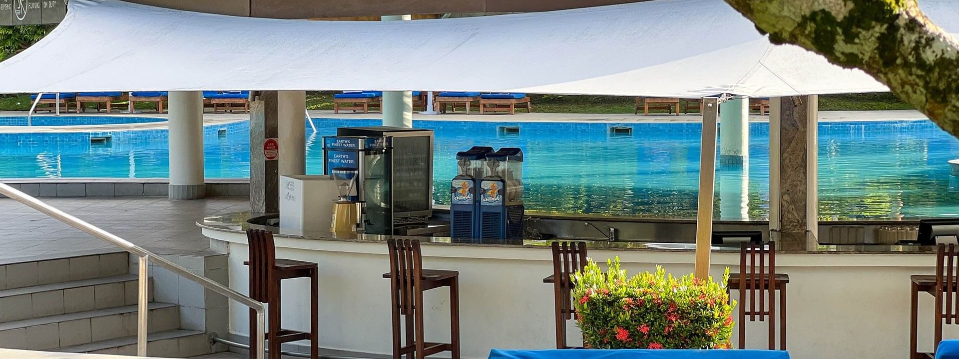 Pool bar under a white canopy with blue lounge chairs in the foreground at The Naviti Resort in Korolevu