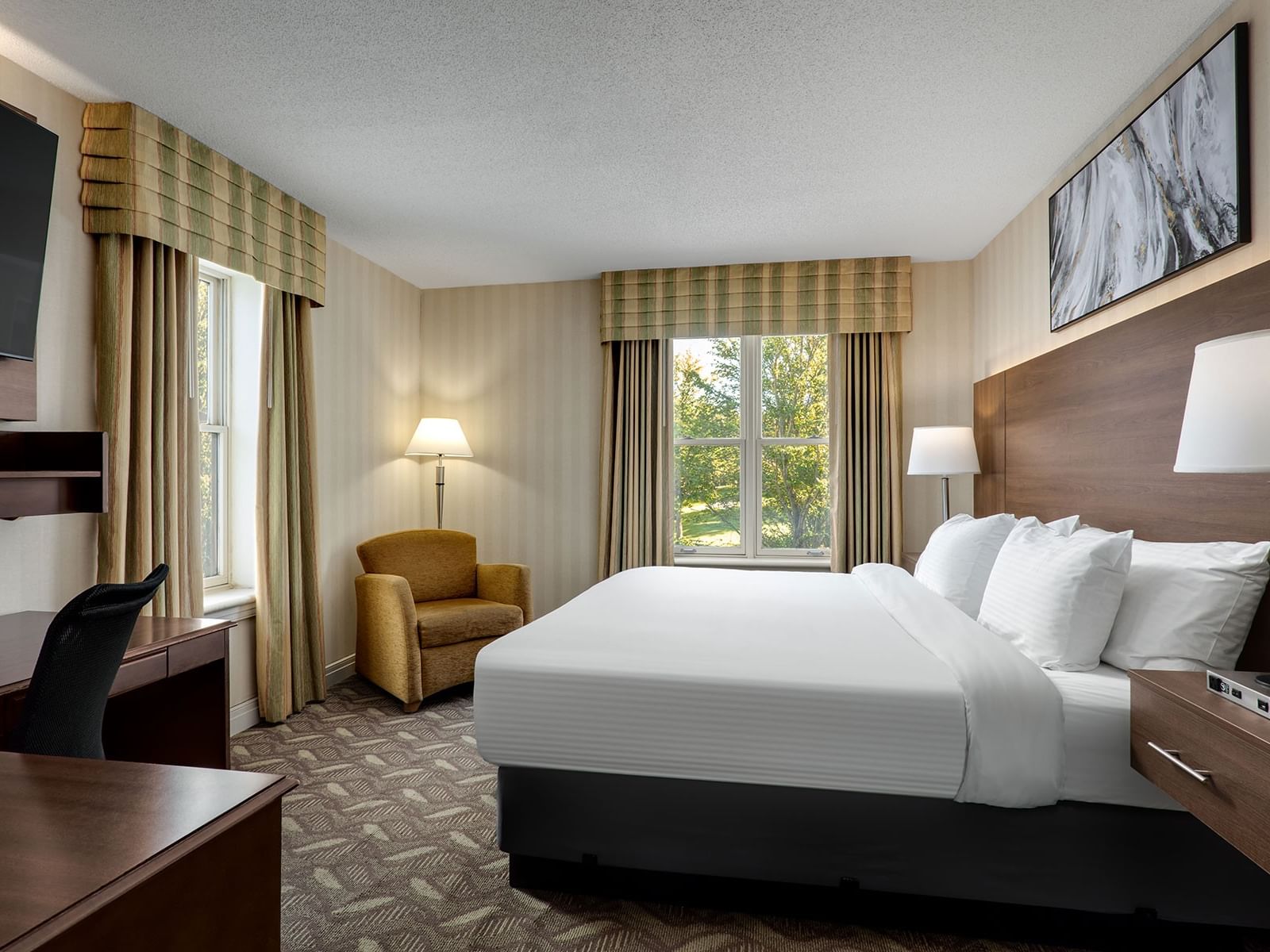 TV with work desk facing bed with couch by window in 1 King Bed Executive Wing at Spencer Hotel & Conference Centre