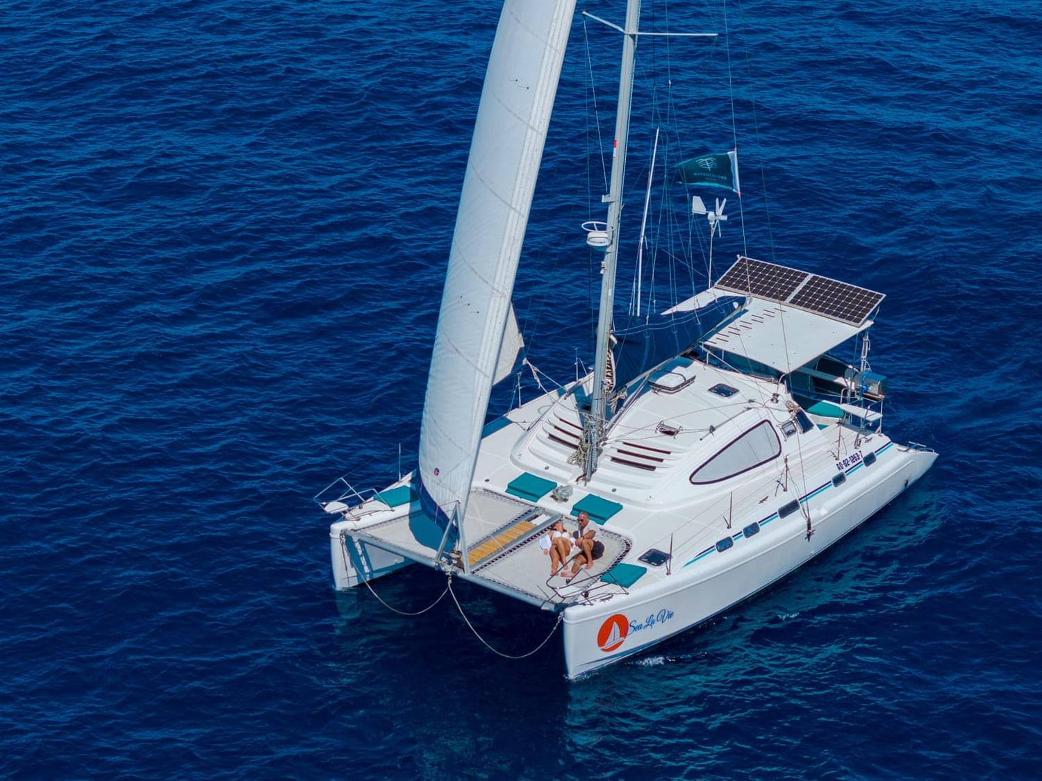 An aerial shot of a white catamaran with two people on board, sailing on the deep blue sea, an activity at Ibagari Hotel
