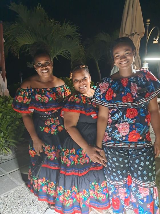 Three women in colorful traditional dresses with floral patterns at Caribbean Night at Windsong Resort On The Reef