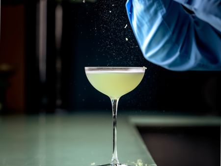 Skilled bartender preparing and garnishing a fresh cocktail at Warwick Hotels and Resorts, with lime zest