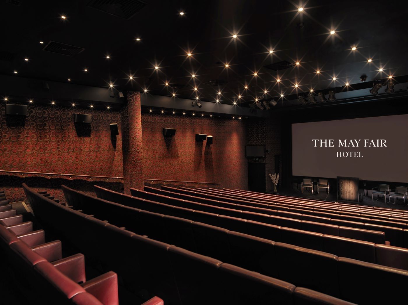 Elegant cinema auditorium with red seating, starlit ceiling, and illuminated screen at The May Fair Hotel, London.