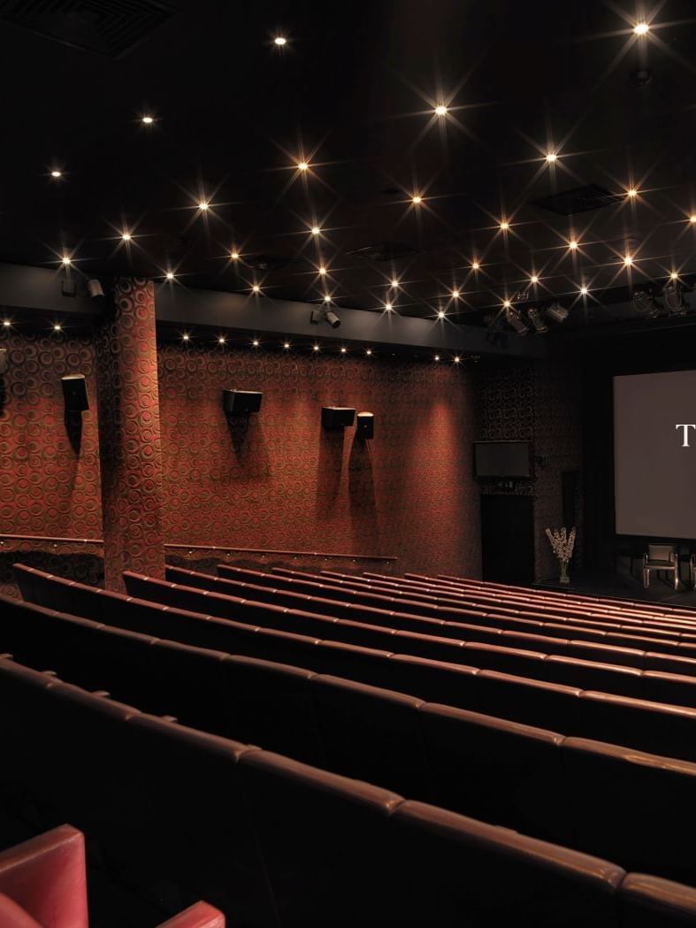 Elegant cinema auditorium with red seating, starlit ceiling, and illuminated screen at The May Fair Hotel, London.