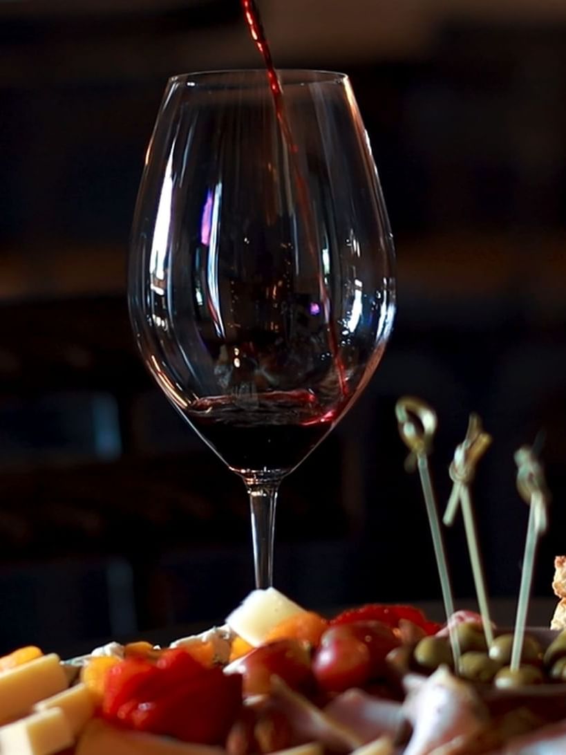 A glass of red wine is being poured above an elegant platter in Brapant bar at El Conquistador Resort