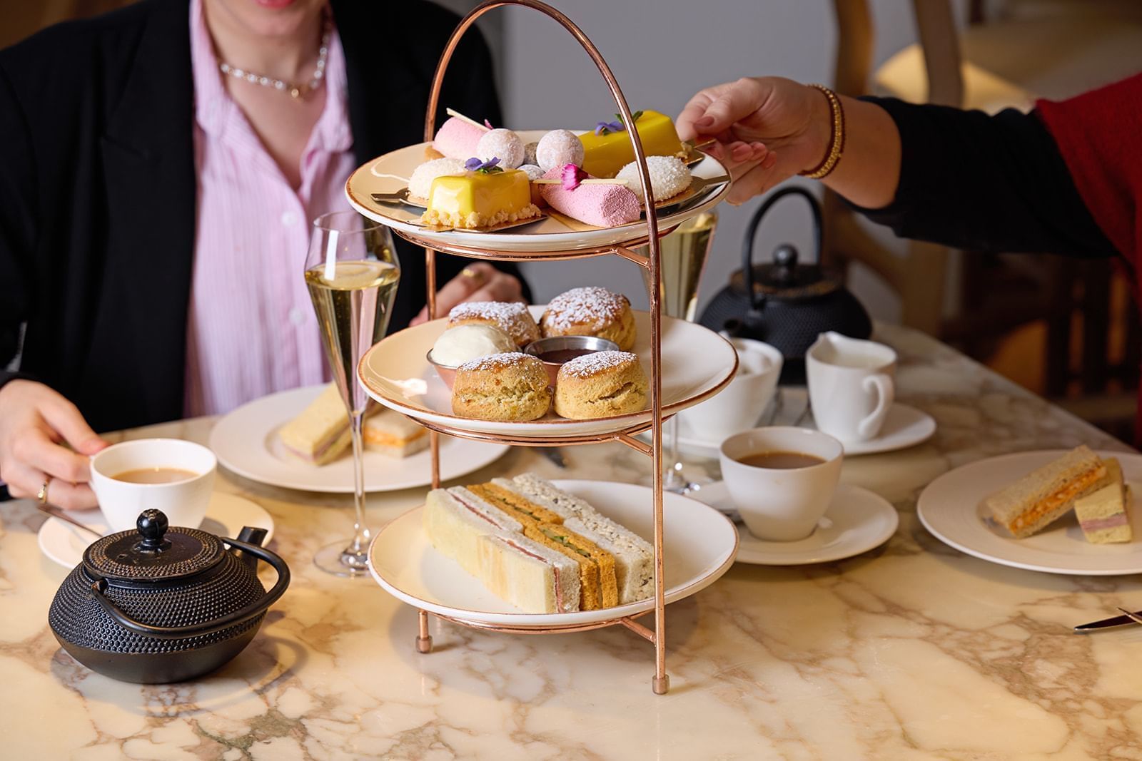 Afternoon tea curated stand with tasty treats, ceramic teapots, cups & champagne served at The May Fair Hotel
