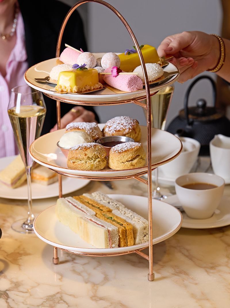 Afternoon tea curated stand with tasty treats, ceramic teapots, cups & champagne served at The May Fair Hotel
