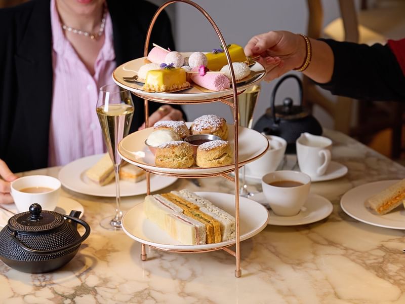 Afternoon tea curated stand with tasty treats, ceramic teapots, cups & champagne served at The May Fair Hotel