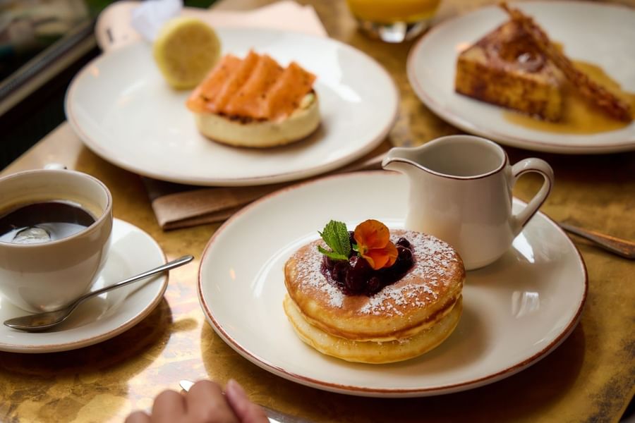 Breakfast table setting with a stack of berry pancakes, a white cup of coffee, and smoked salmon at The May Fair Hotel