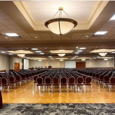 Rows of maroon chairs facing a screen, under pendant lighting on a wood parquet floor at Glenmore Inn & Convention Centre