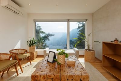 Living room interior with a wooden coffee table, large window, and indoor plants at The Terraces Resort & Spa