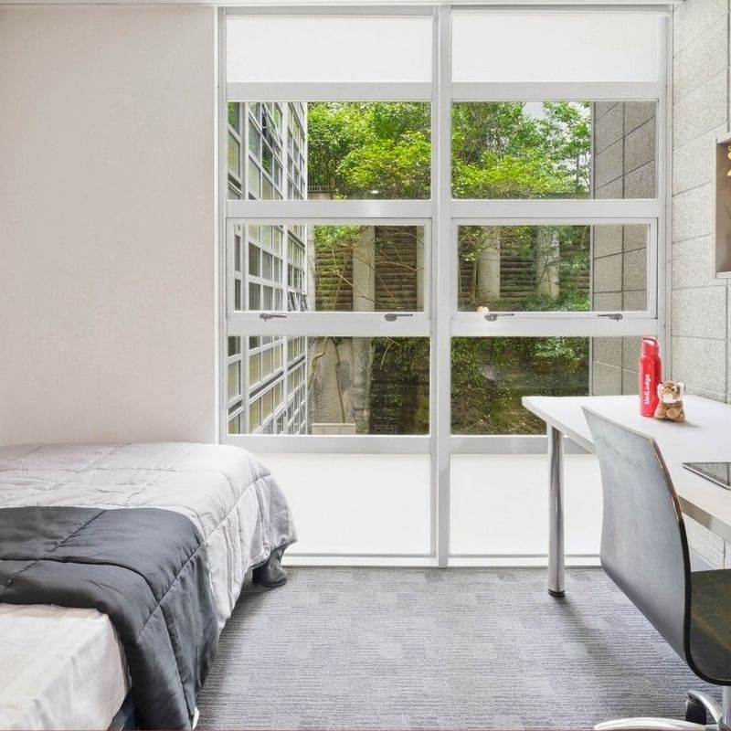 Bedroom with bed, desk, chair, and large window at Student Living Auckland - Beach.