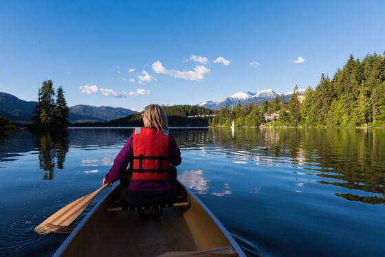 Woman canoeing on a lake with mountain backdrop near Blackcomb Springs Suites