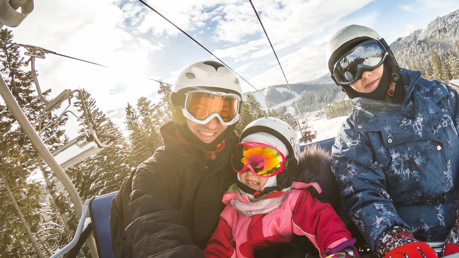 Three people on a ski lift with surrounded by snowy mountains at Listel Whistler, a Coast Hotel