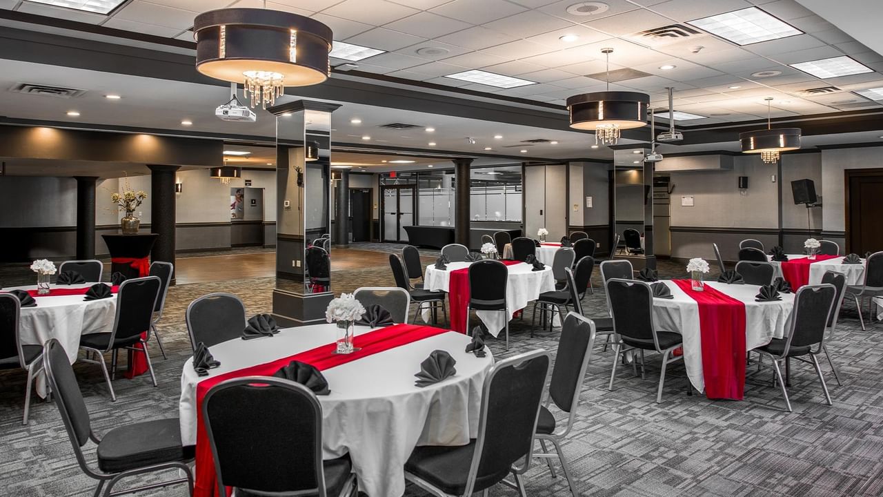 Event space with round tables dressed in white linens and red runners, black chairs, and elegant chandeliers.