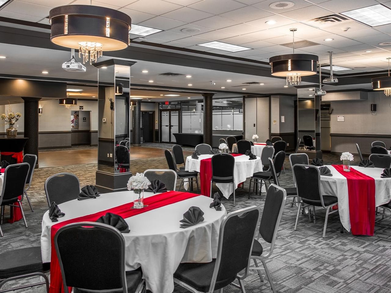 Event space with round tables dressed in white linens and red runners, black chairs, and elegant chandeliers.