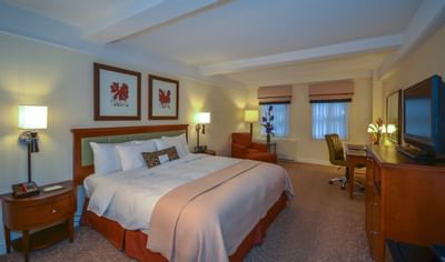 Hotel room with large bed, nightstands, armchair, desk, and TV setup, showcasing a comfortable and furnished interior.