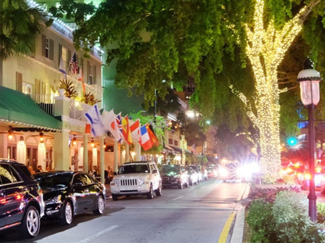 A vibrant street scene at night, adorned with twinkling lights on trees and flags lining Riverside Hotel Fort Lauderdale