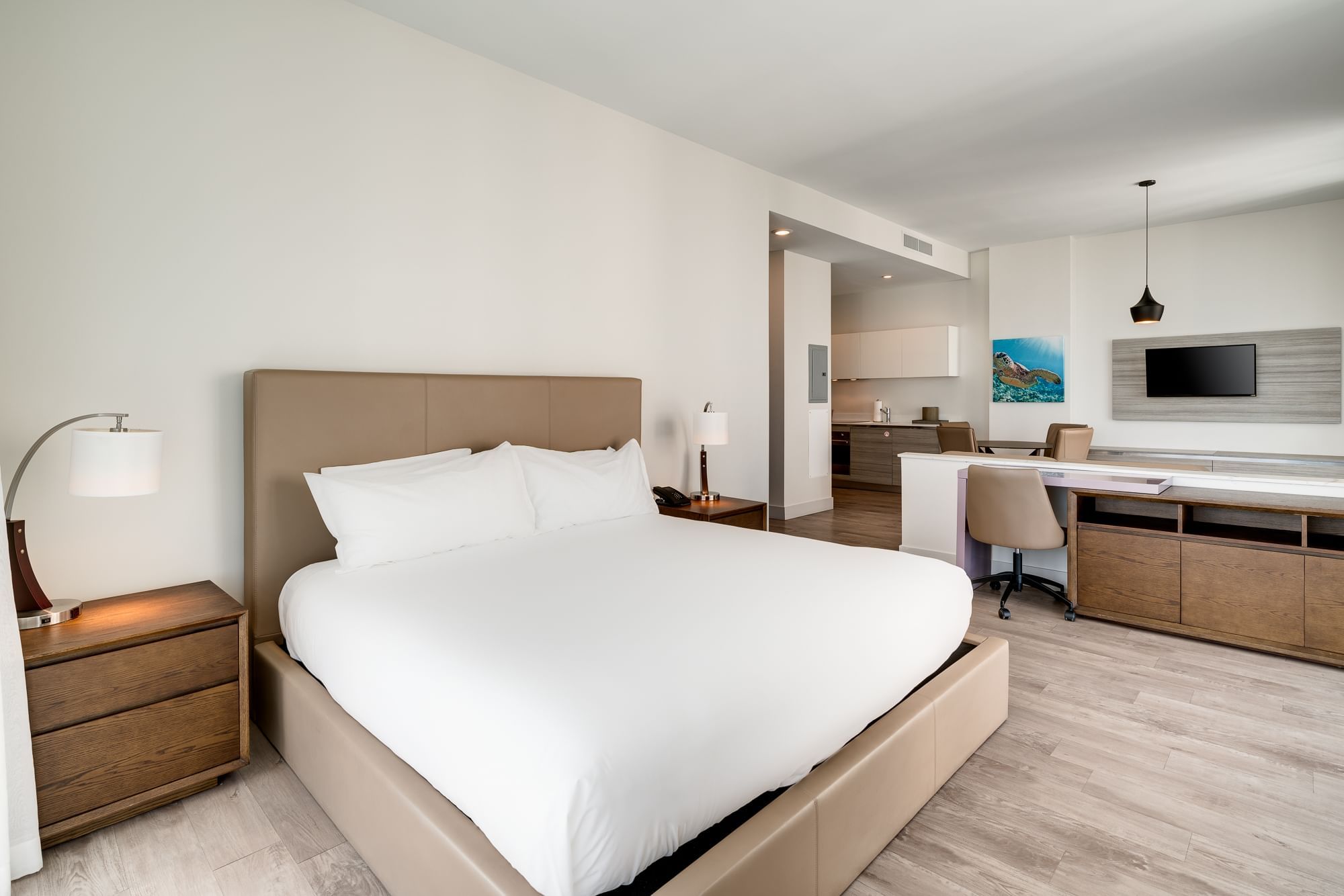 A modern hotel room with a large bed, desk area, and kitchenette.