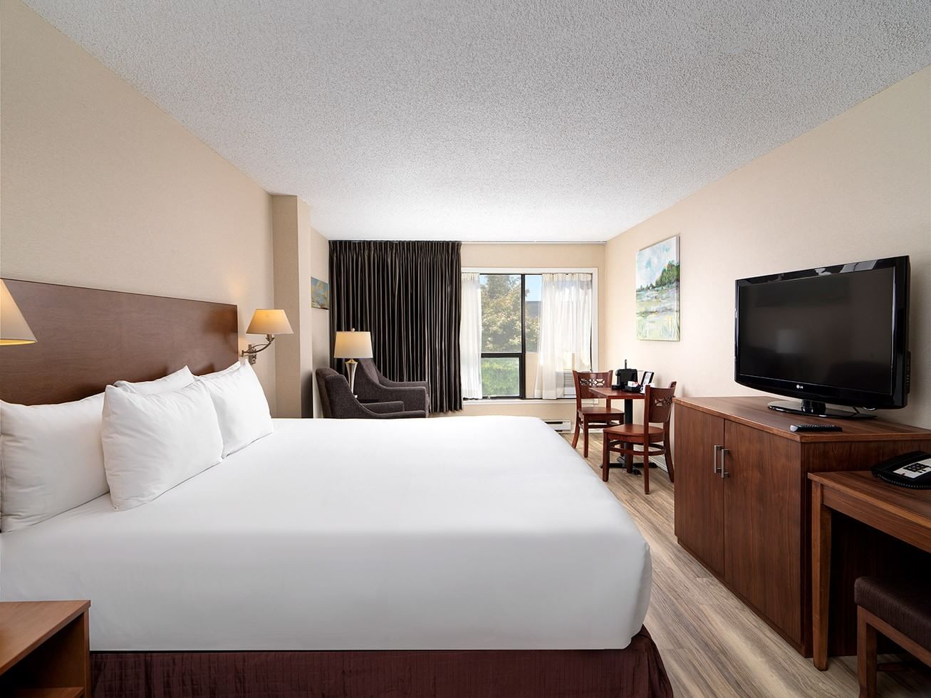 Hotel room with large bed, TV on cabinet, desk, and dining area with chairs and table.