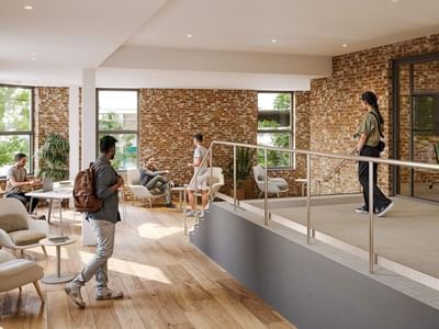 A modern office space with people, brick walls, wooden floors, and a balcony with a metal railing.