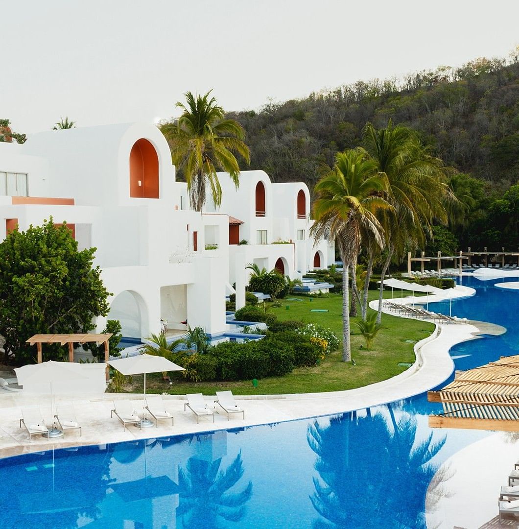 Outdoor pool area with sun loungers and patio umbrellas, surrounded by lush greenery at Camino Real Zaashila Huatulco