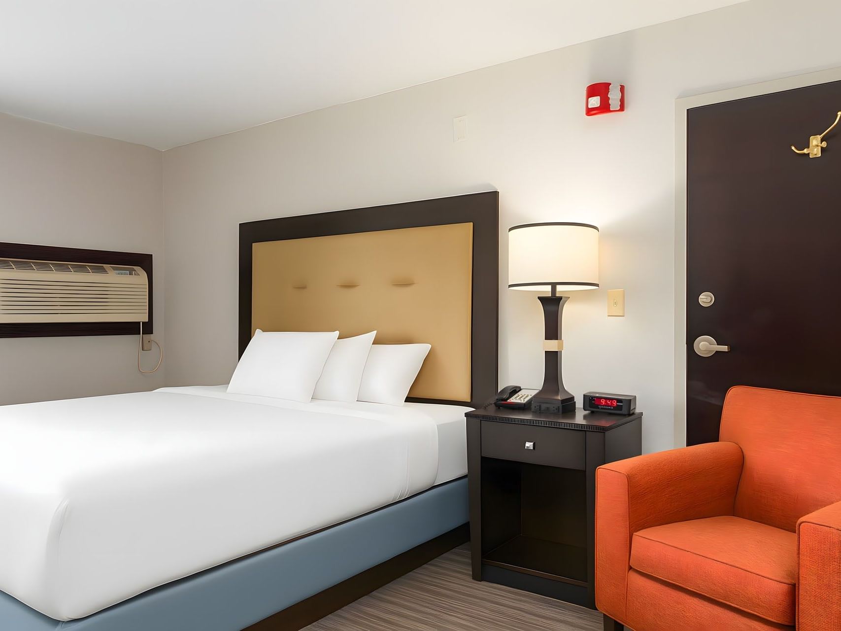 Standard King Room bed with plush white linens next to a dark wood nightstand and orange armchair at Branson Hillside Hotel