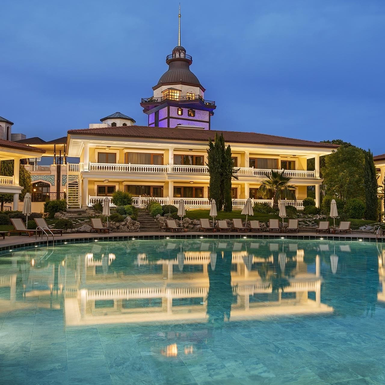 Luxuriöses Lake House mit Pool und Liegestühlen zwischen Bäumen unter dem nächtlichen Himmel.