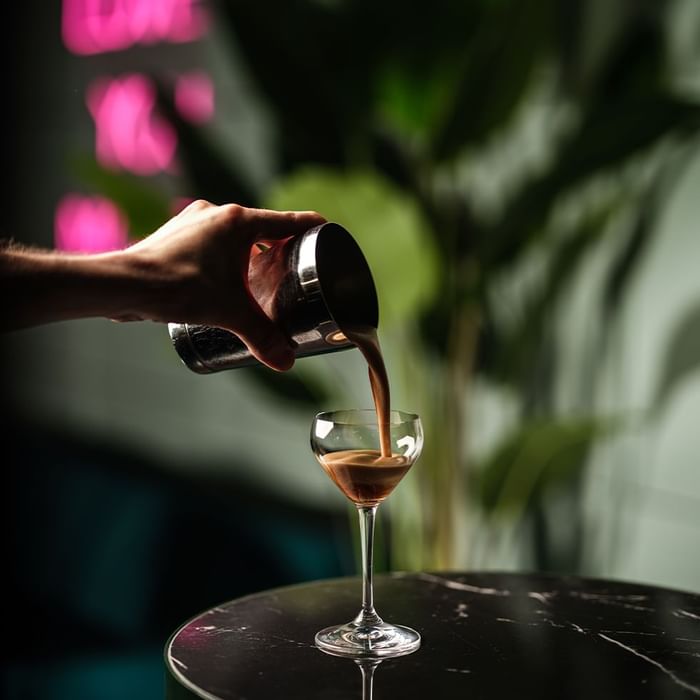 Hand pouring a dark liquid into a cocktail glass in The Monkey Bar at Falkensteiner Hotel Prague