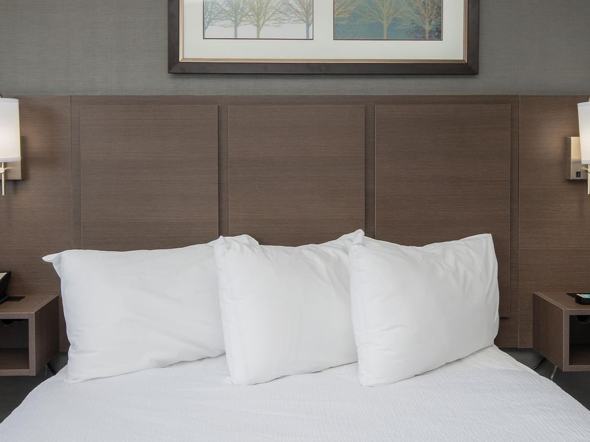 Three pillows on a bed with nightstands and wall lamps.