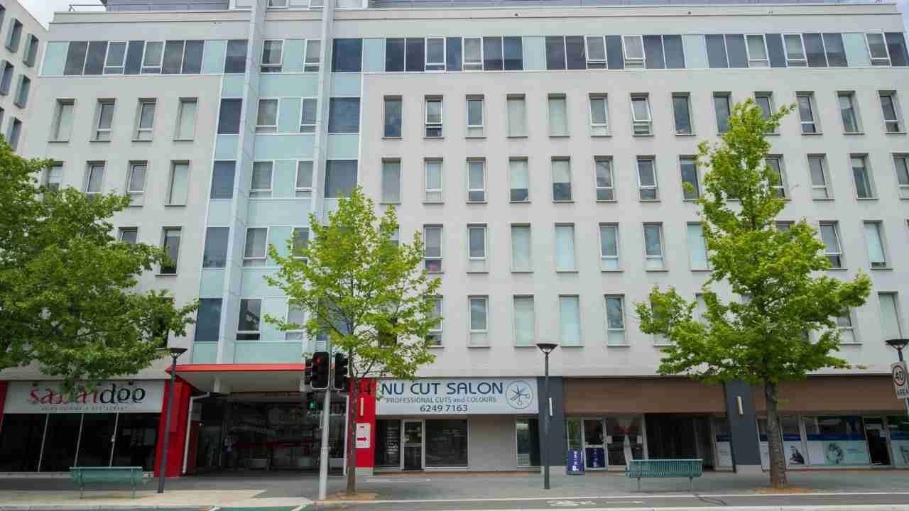 Exterior of Student Living Academie House building with storefronts and trees.