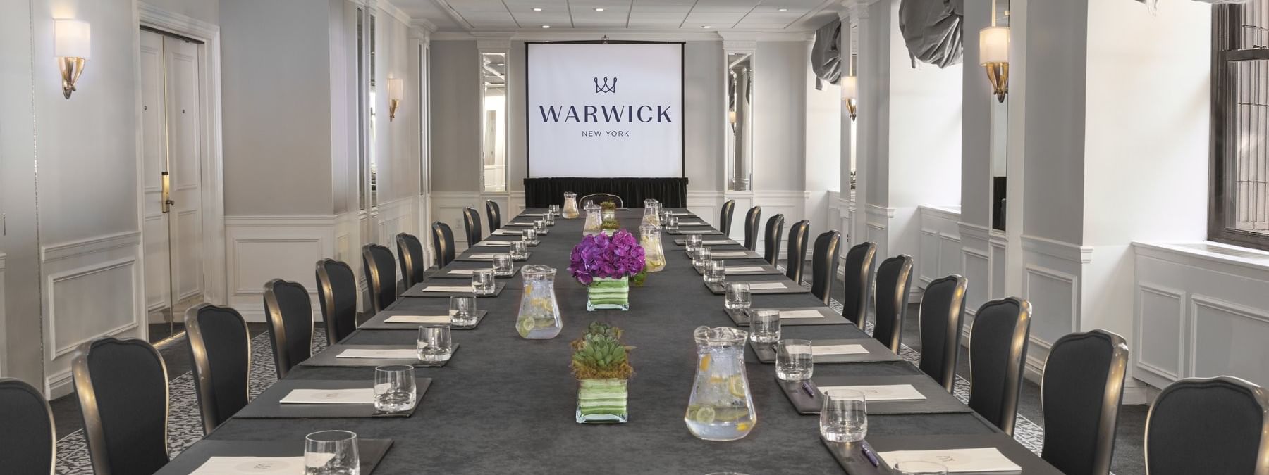 Close-up of a long conference table with purple flowers & glass sets in Essex meeting room at Warwick New York