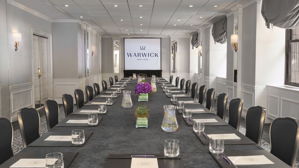 Close-up of a long conference table with purple flowers & glass sets in Essex meeting room at Warwick New York